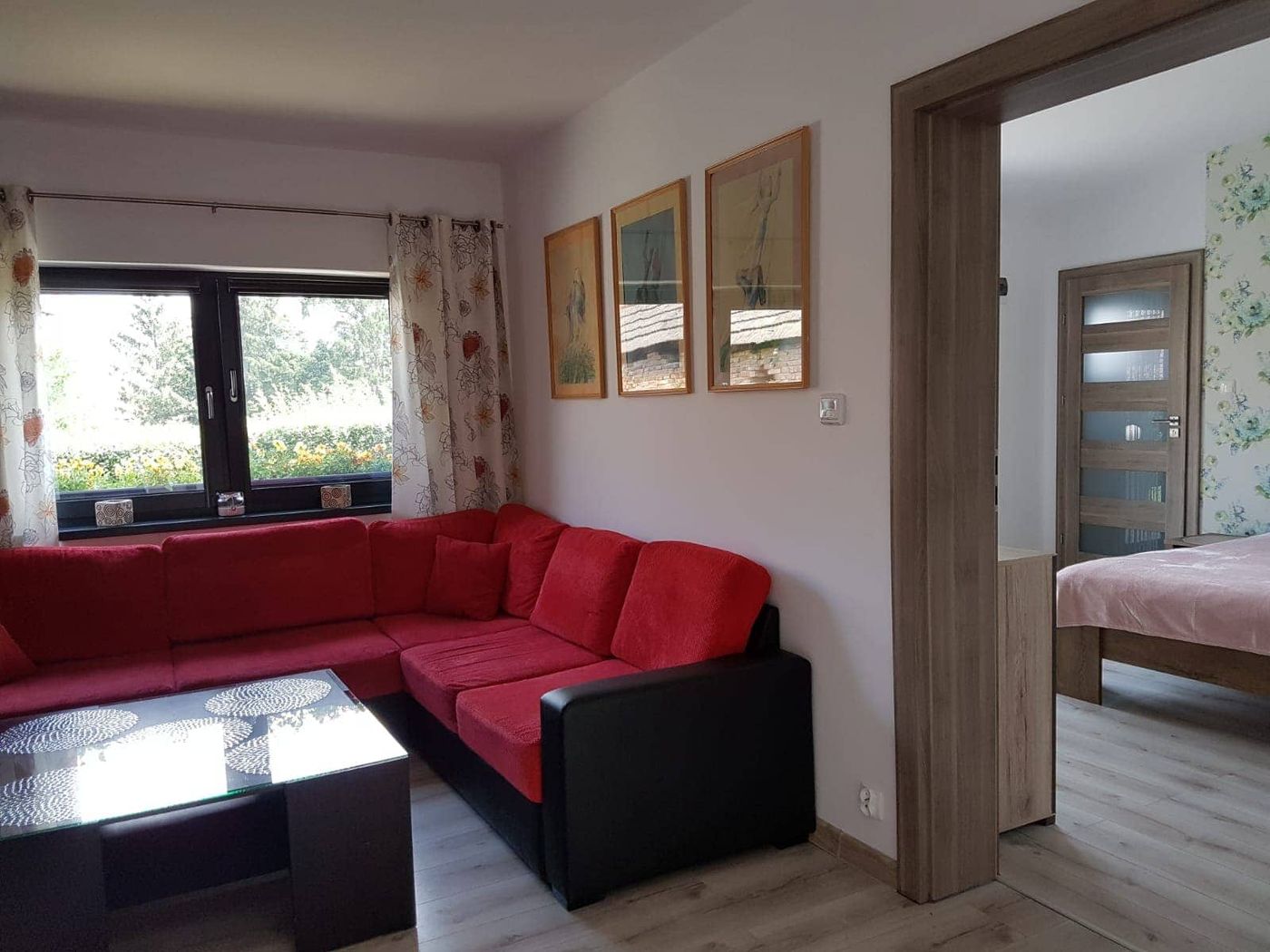 Salon apartamentu z czerwonym narożnikiem i przejściem do sypialni