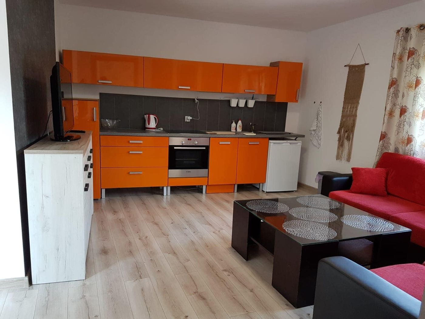 Aneks kuchenny apartamentu w pomarańczowej zabudowie z piekarnikiem i telewizorem