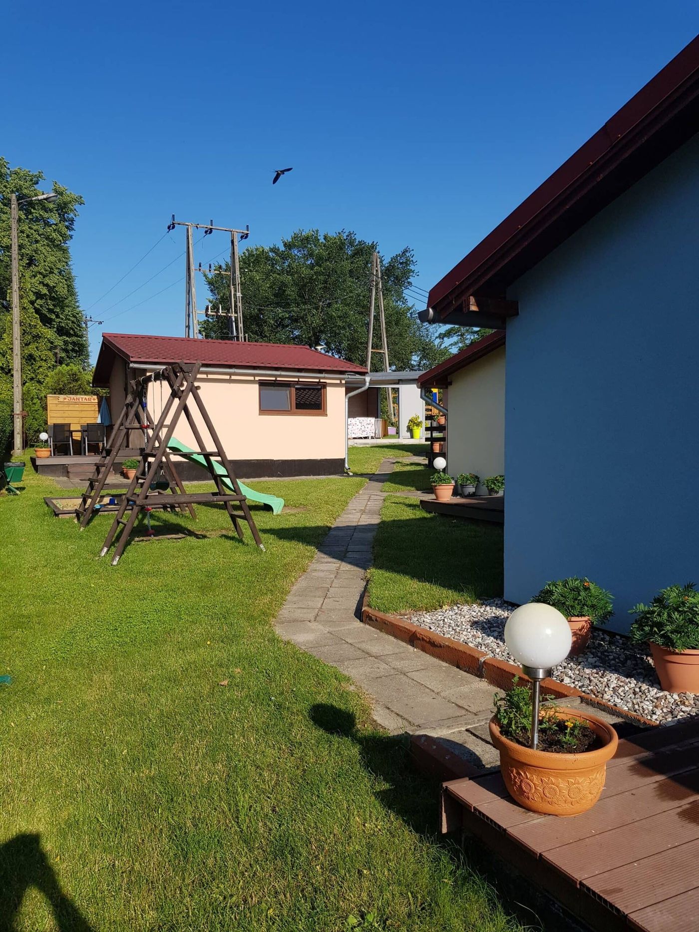 Plac zabaw z huśtawką i zjeżdżalnią pomiędzy domkami ośrodka