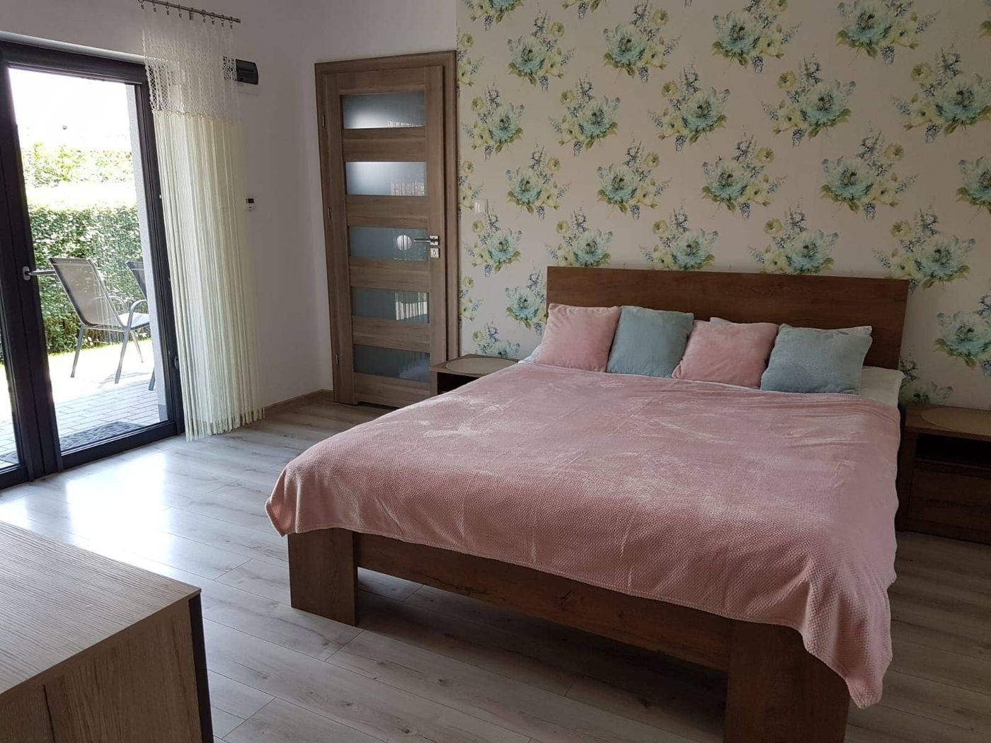 Sypialnia apartamentu z dużym drewnianym łóżkiem i wyjściem na taras